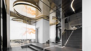 Un interior moderno con paredes de vidrio, una escalera y una gran obra de arte iluminada.