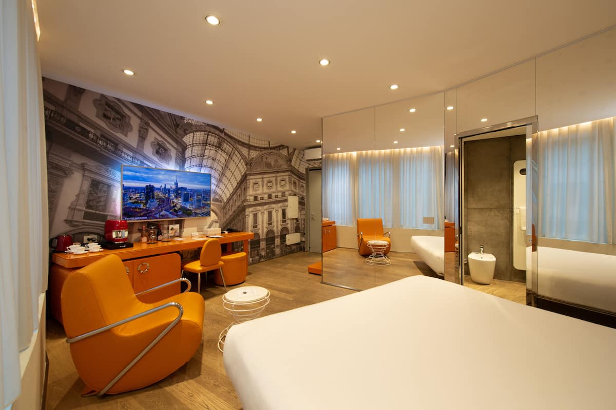 Una habitación de hotel moderna con una cama grande, un escritorio con silla, un sofá y un espejo amplio.