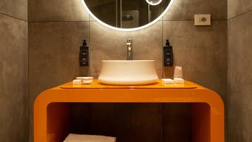 A modern bathroom with a round mirror, a white sink, and an orange vanity.