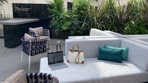 Un espacio al aire libre con sofás, sillas y un ordenador portátil sobre una mesa.