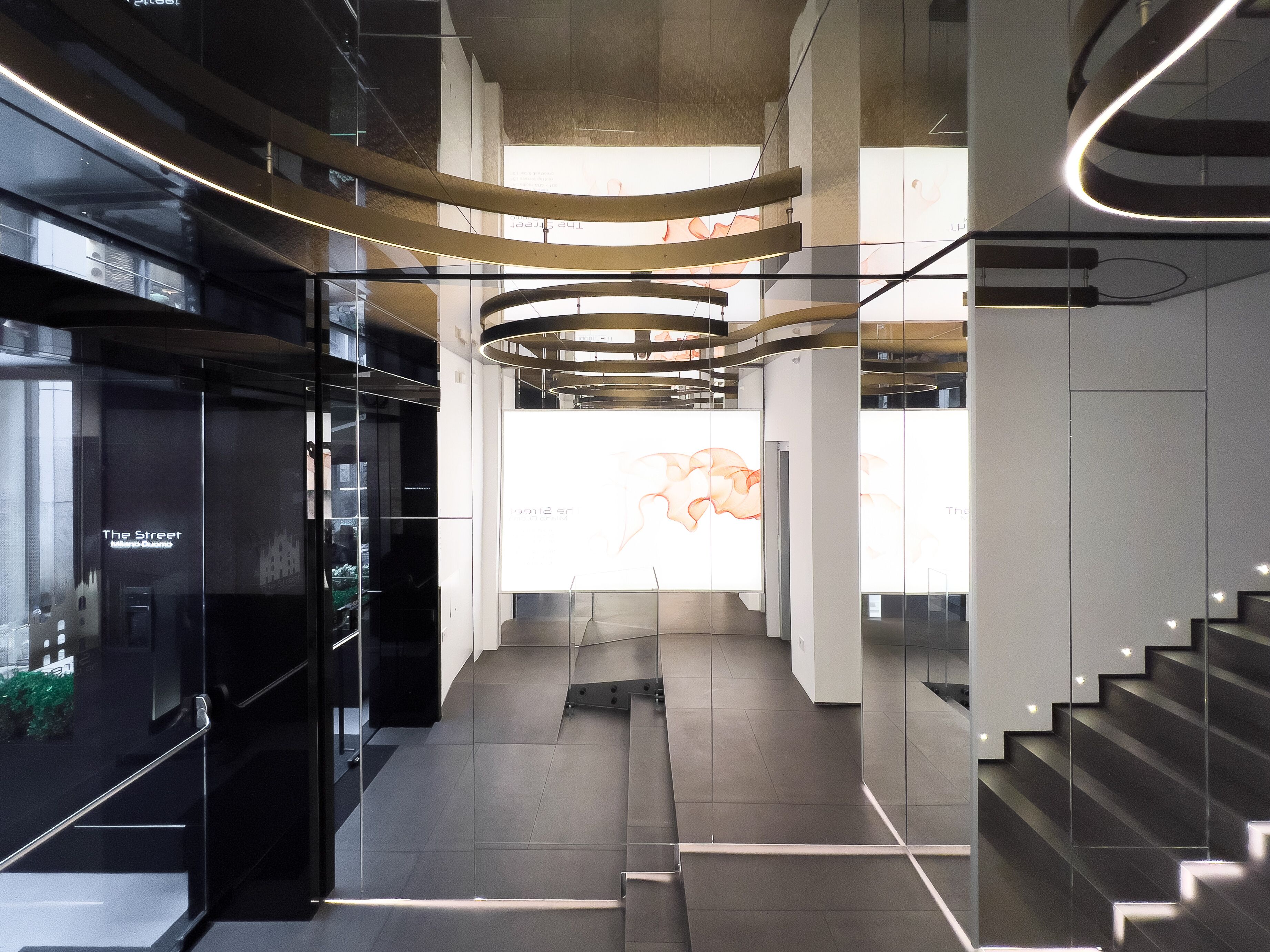 Un interior moderno con fachada de vidrio, una escalera y una lámpara central.
