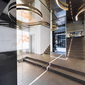 Un interior moderno con una escalera de cristal, una pared con una exhibición de arte digital y una zona de recepción.