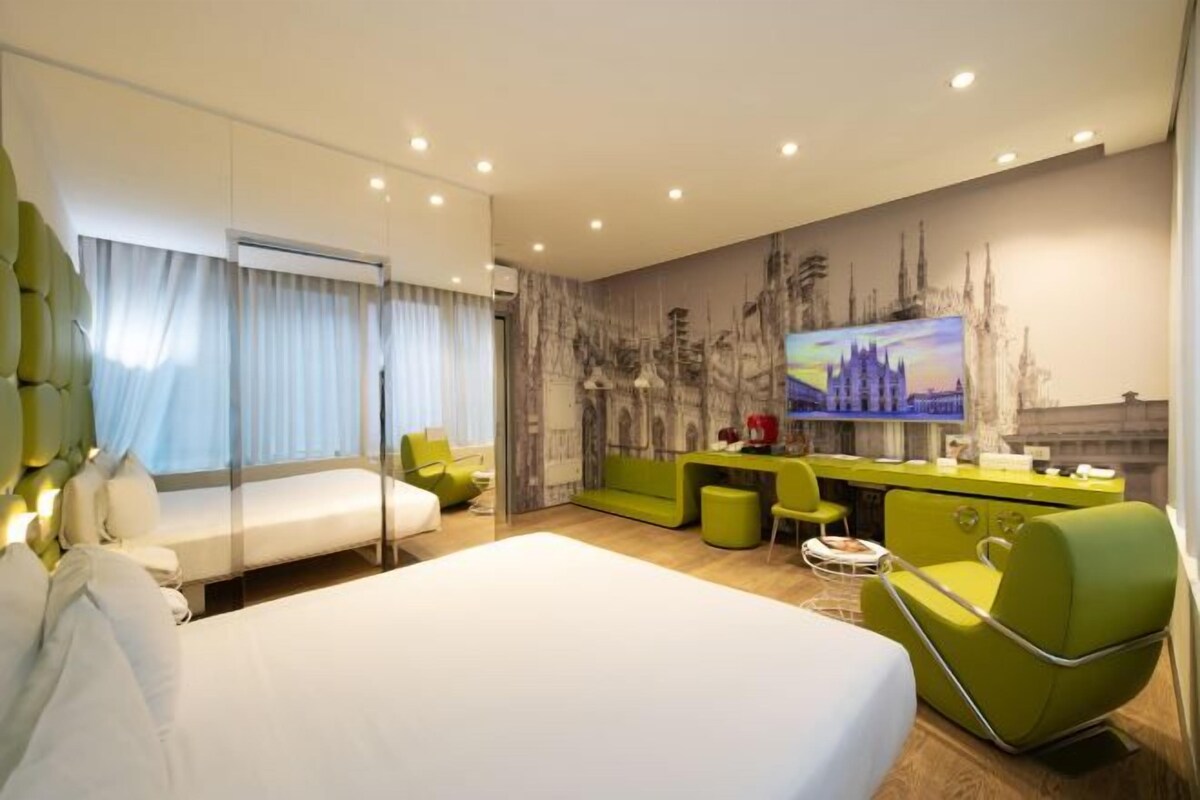 Ein modernes Hotelzimmer mit einem großen Bett, einem Schreibtisch mit Stuhl, einer Couch und einem Fernseher.