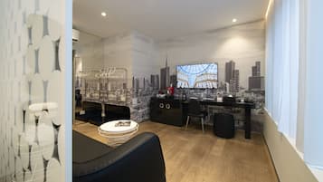 Een moderne woonkamer met een stadsgezicht op de muur, een zwarte leren bank, een ronde salontafel en een bureau met een computer.