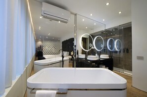 Une salle de bain moderne avec une grande baignoire, un miroir doté de lumières disposées en cercle et une cloison en verre.