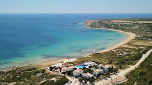 Luftaufnahme eines Küstenresorts mit Schwimmbad, Strand und einer Straße, die zu den Gebäuden führt.