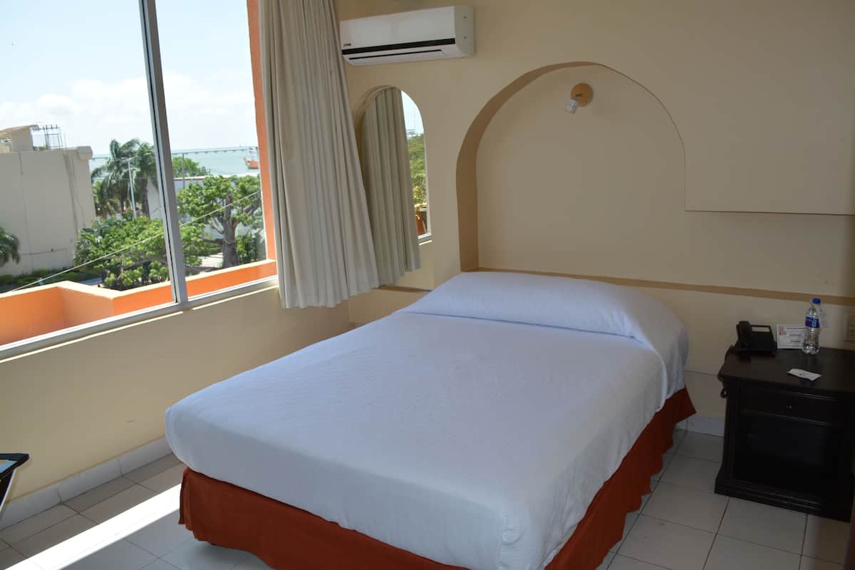 Une chambre d’hôtel équipée d’un lit, d’une table de chevet, d’un appareil de climatisation et d’une fenêtre avec des rideaux.