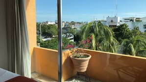 Habitación de hotel con un ventanal grande, una cama, una planta en maceta y vistas de la ciudad.