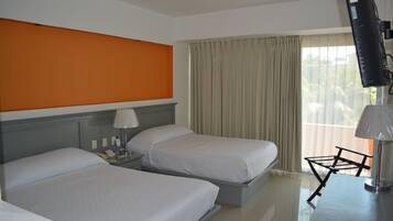 A hotel room with two beds, a television, and a window with curtains.