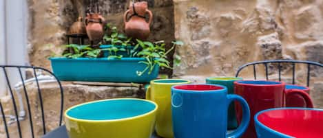 A table with colorful ceramic mugs and bowls, a hanging pot rack, and a potted plant.