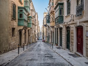 Una calle estrecha flanqueada por edificios históricos, con balcones, una puerta roja y cielo despejado.