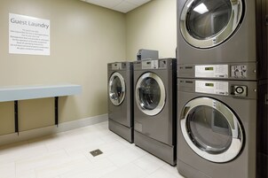 Un área de lavandería con varias secadoras LG comerciales, un letrero para huéspedes y un banco blanco.