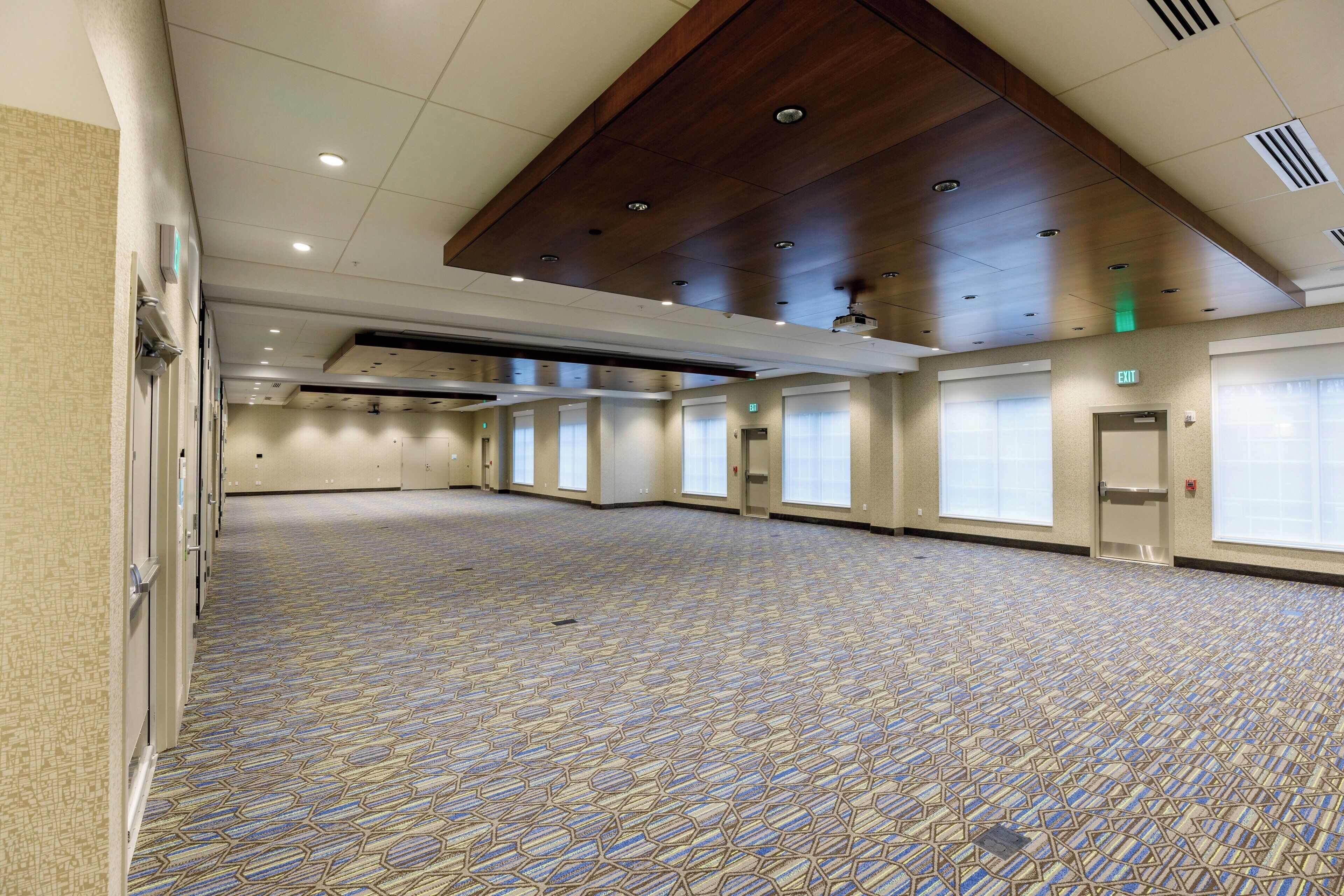 A large, empty conference room with a patterned carpet, multiple windows, and a high ceiling with recessed lighting.