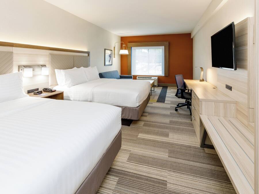 Ein Hotelzimmer mit zwei Betten, einem Schreibtisch, einem Sessel, einem Fernseher und einem Fenster.