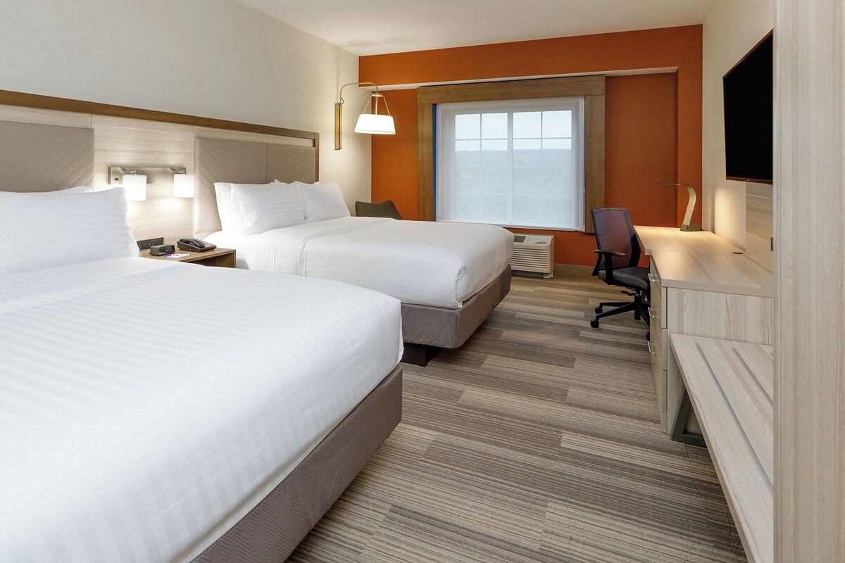 A hotel room with two beds, a desk, a chair, a TV, and a window.