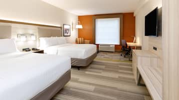 A hotel room with two beds, a desk, a chair, a TV, and a window.