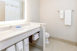 A modern bathroom with a white sink, mirror, and toilet. There are two towels hanging on a rack and a shelf with folded towels below the sink. - Holiday Inn Express & Suites Sturbridge by IHG (Sturbridge)