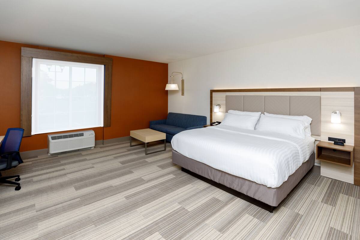 A hotel room with a large bed, a desk, a chair, and a window.