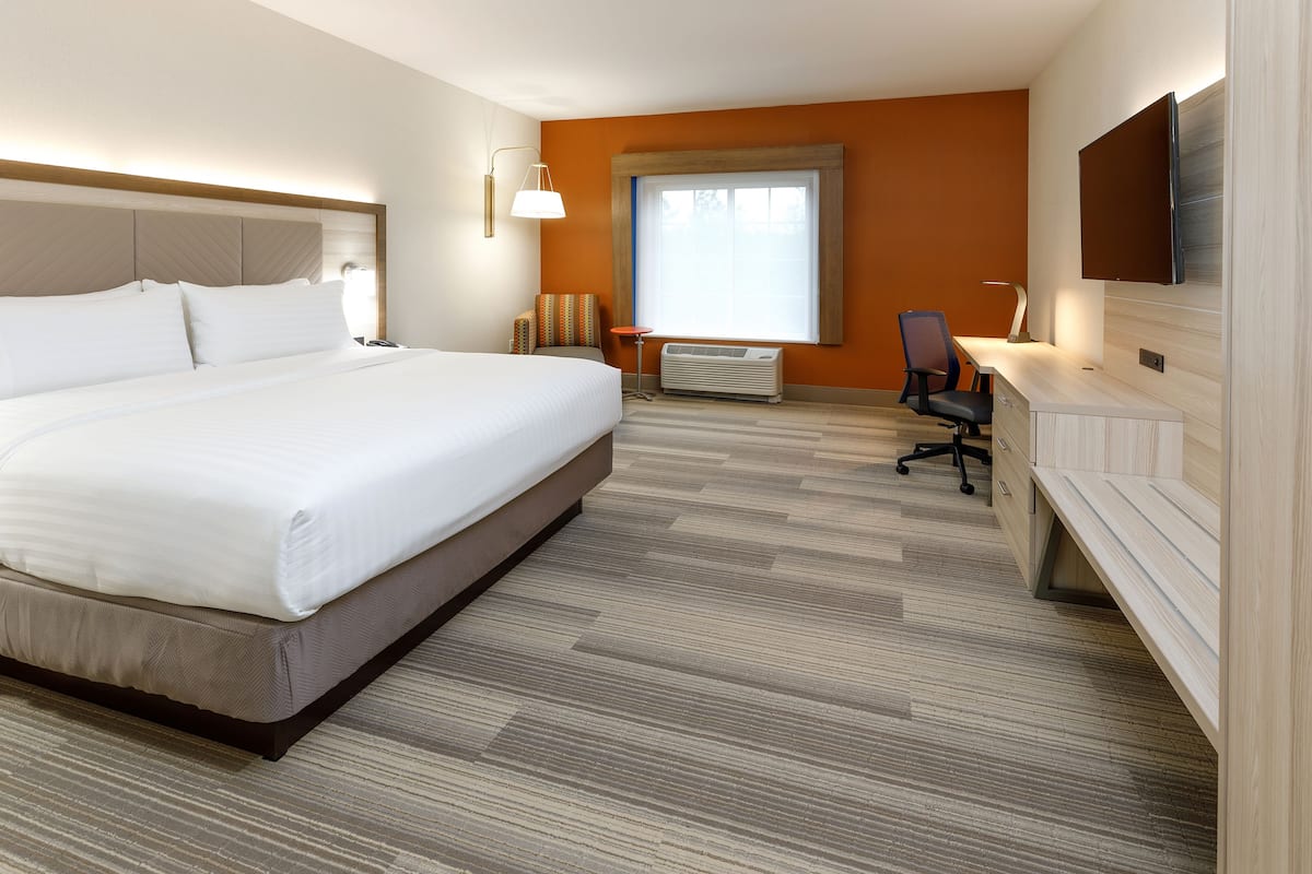 A hotel room with a large bed, a desk, a chair, a flat-screen TV, and a window with blinds.
