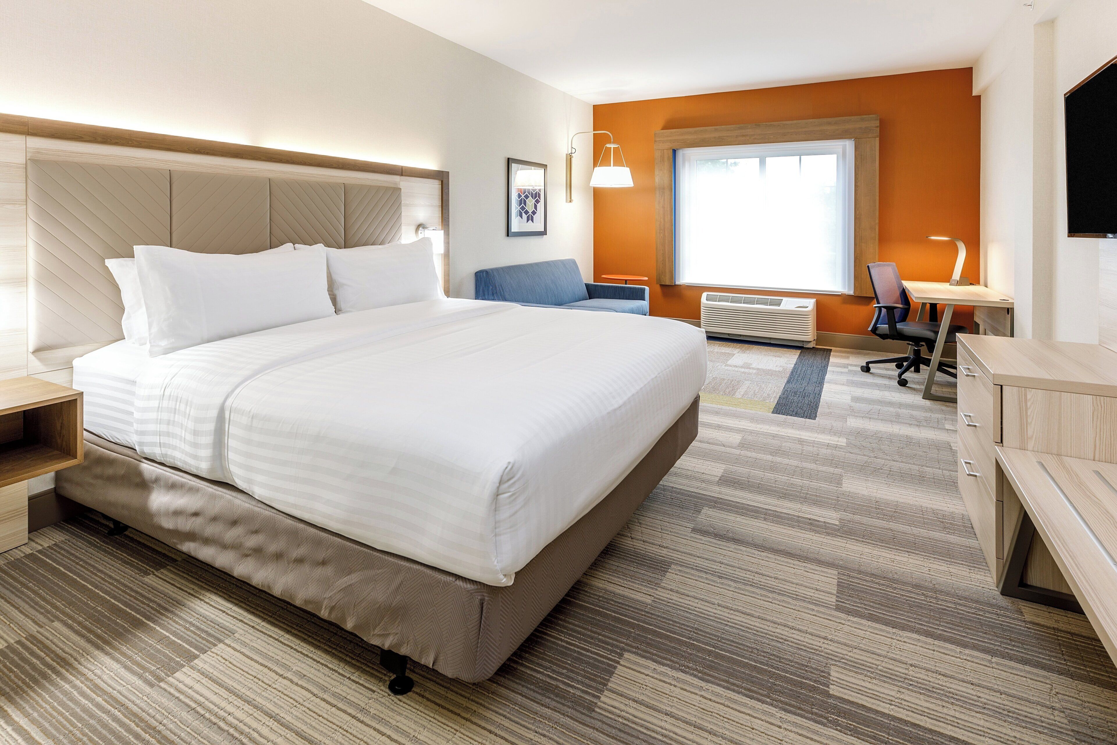 A hotel room with a large bed, a desk, a chair, and a window.