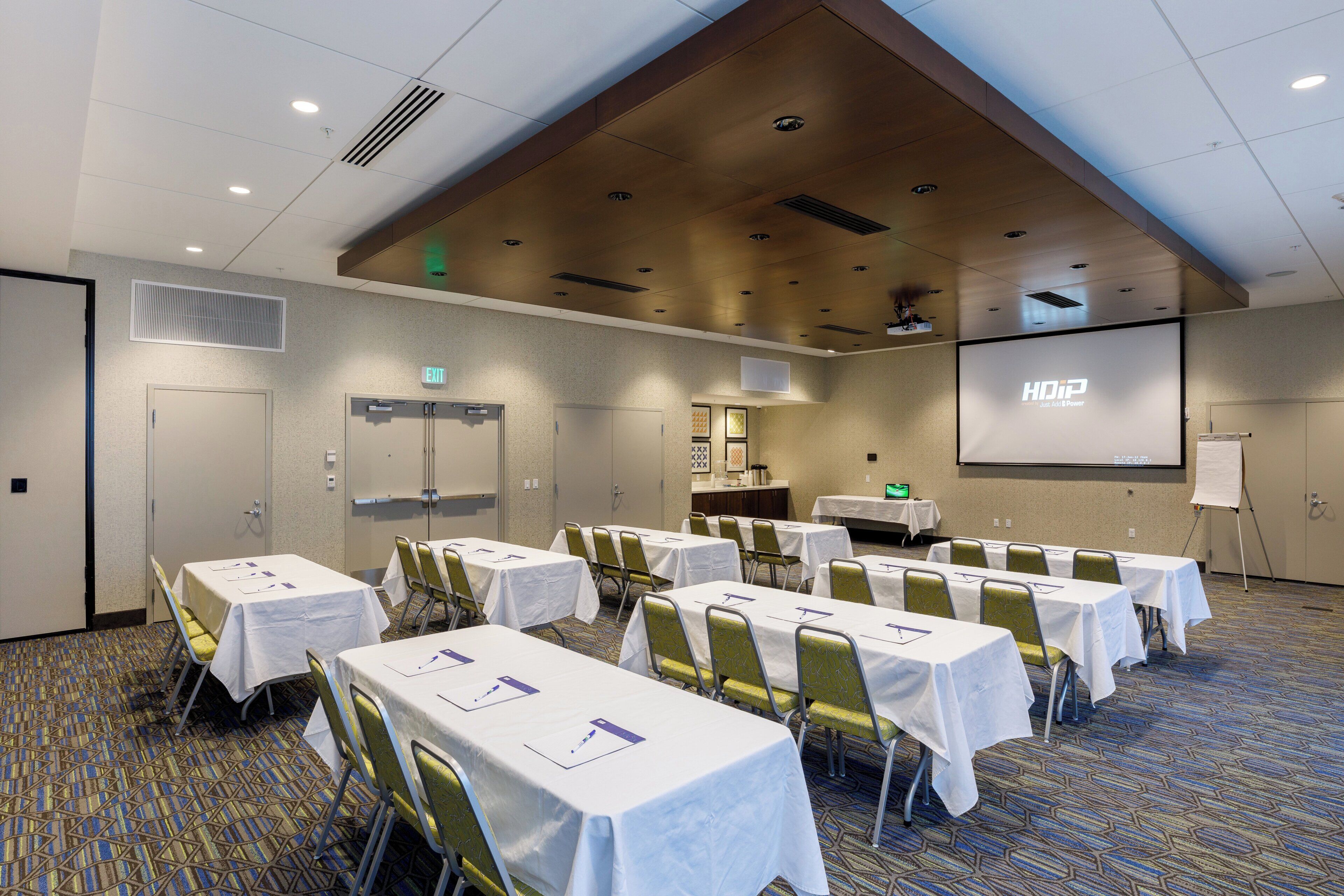 A conference room with tables, chairs, a projector screen, and a presentation screen.