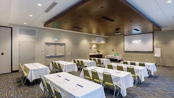 A conference room with tables, chairs, a projector screen, and a presentation screen.
