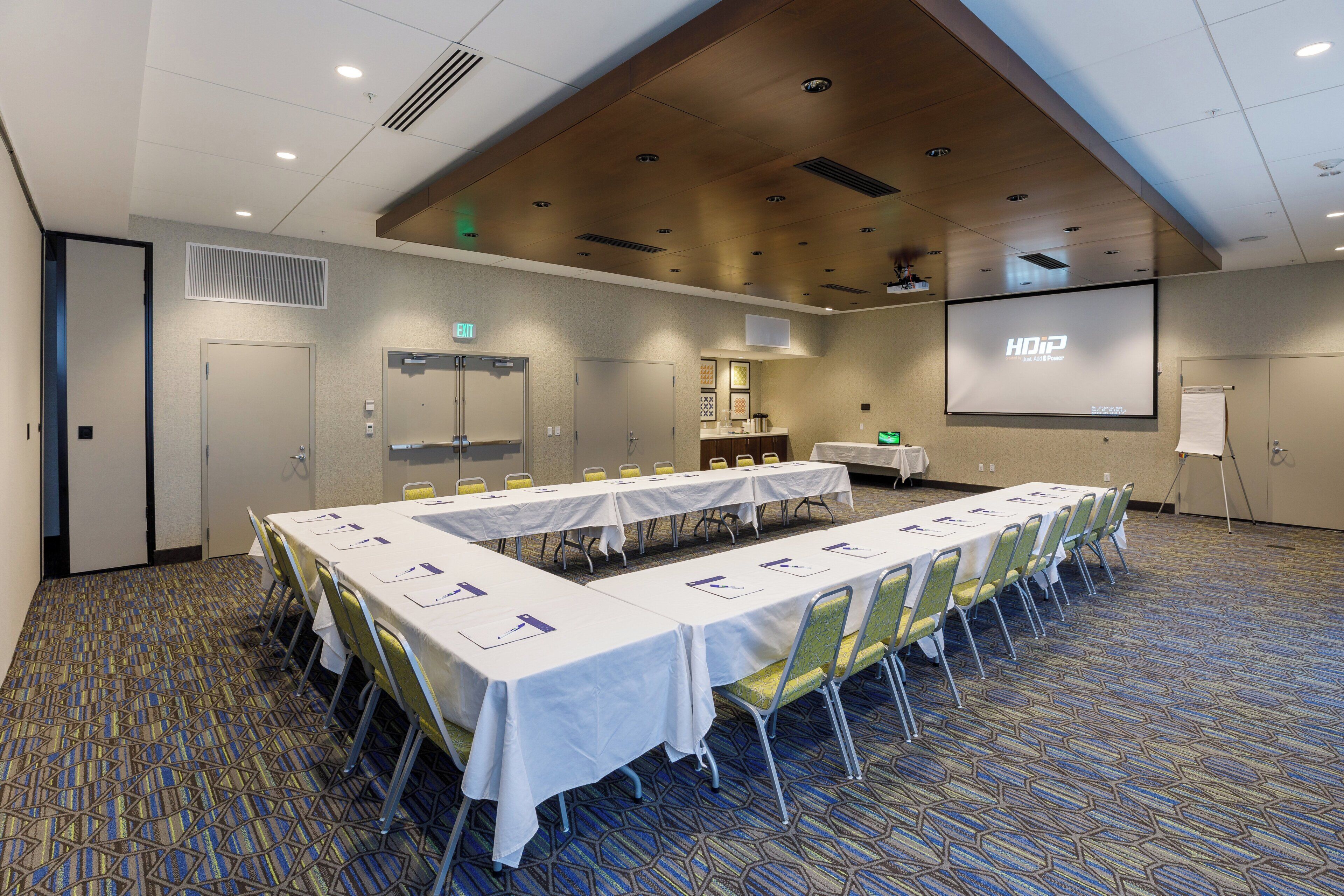 Un salón de conferencias con una mesa larga, sillas, una pantalla de proyector y una señal de salida.