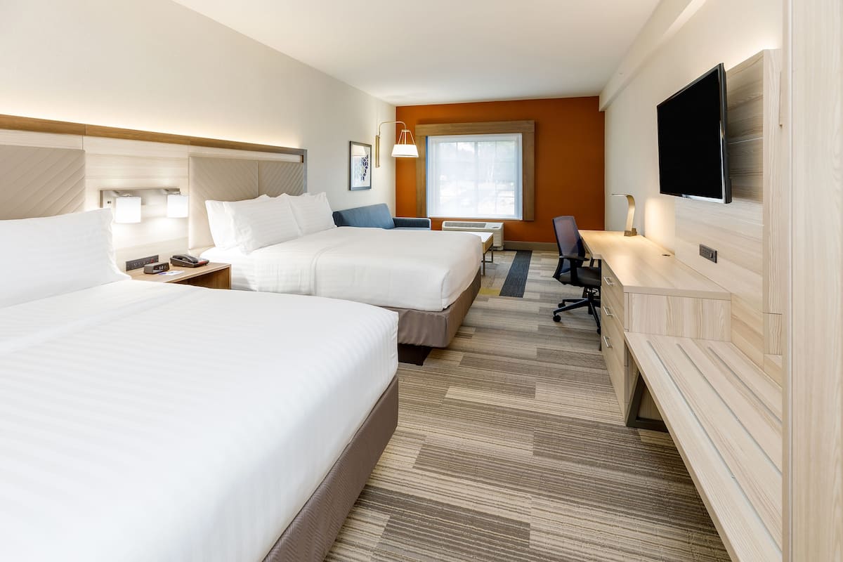 A hotel room with two beds, a desk, a chair, a flat-screen TV, and a large window.