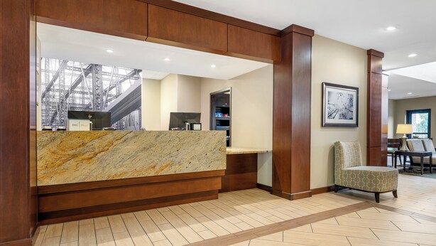 A reception area with a marble counter, wooden paneling, a framed picture on the wall, and a patterned floor. - Staybridge Suites Pittsburgh-Cranberry Township by IHG (Warrendale)
