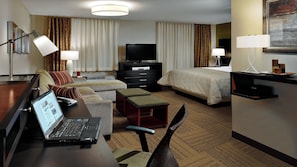 Une chambre d’hôtel avec un lit, un bureau avec un ordinateur portable, une télévision et une table de chevet.