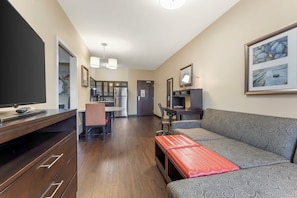 Un espace de vie compact comprenant un canapé, un téléviseur, un coin repas et une kitchenette.