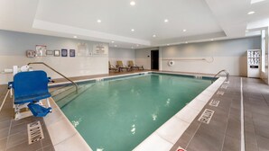 An indoor swimming pool with a lifeguard chair, lounge chairs, and safety signs.