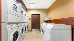 A laundry room with multiple washing machines and dryers, wooden walls, and a tiled floor.