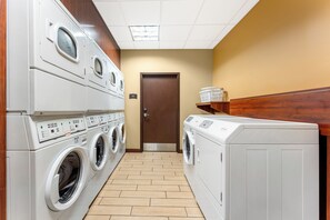 Un cuarto de lavado con varias lavadoras y secadoras, paredes de madera y piso de baldosas.