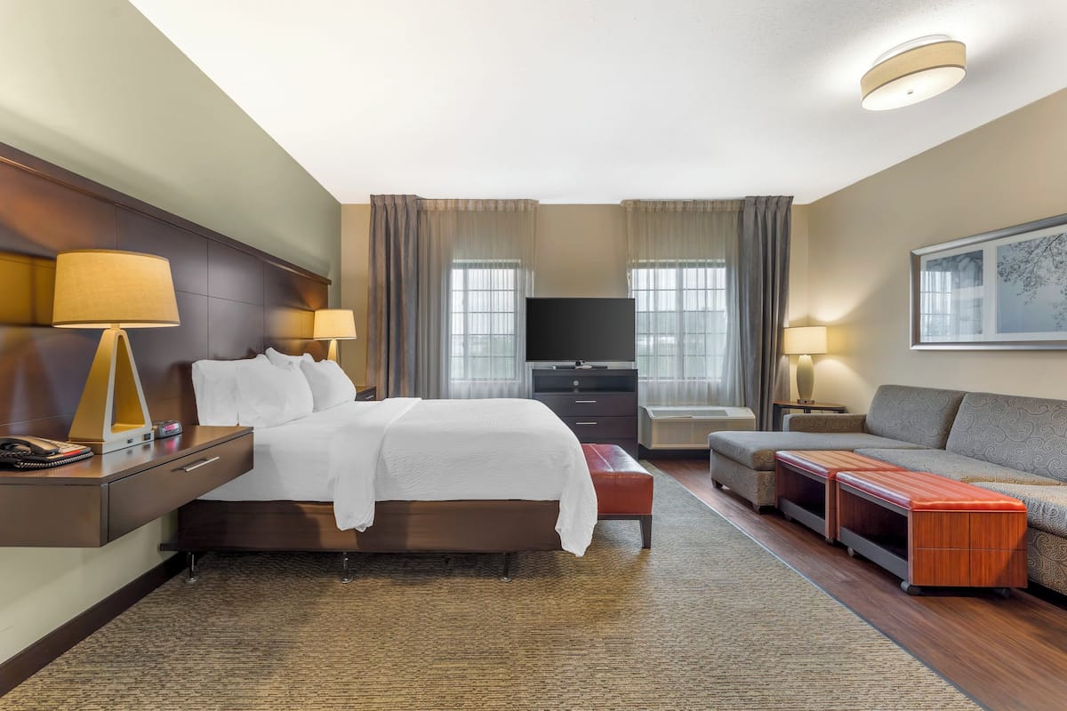 A hotel room with a bed, a TV, a sofa, and a desk with a lamp.