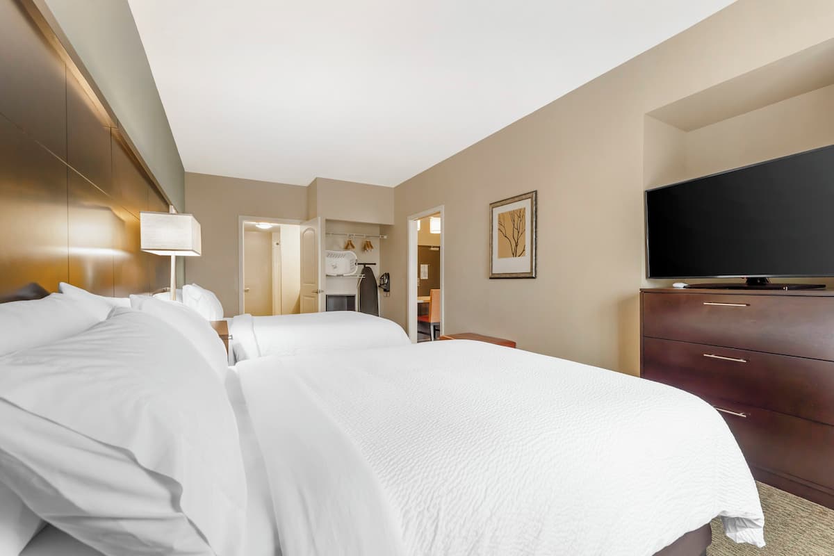 A hotel room with two beds, a TV, a dresser, and a bathroom visible through an open door.