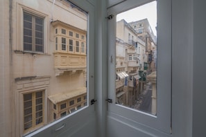 A view through a window of a building with multiple stories, featuring traditional architectural elements such as balconies and detailed window frames. - Kursara (Valletta)