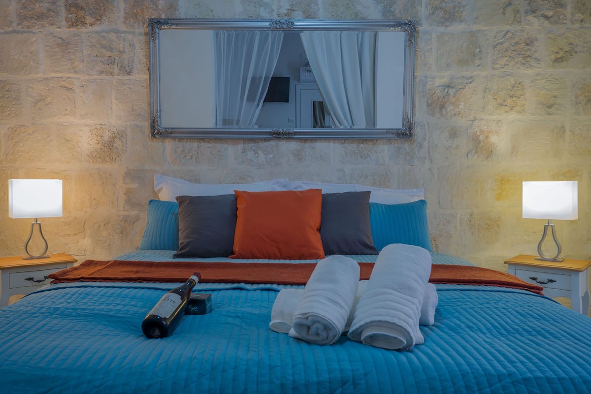 A neatly made bed with blue bedding, a bottle, and rolled towels.