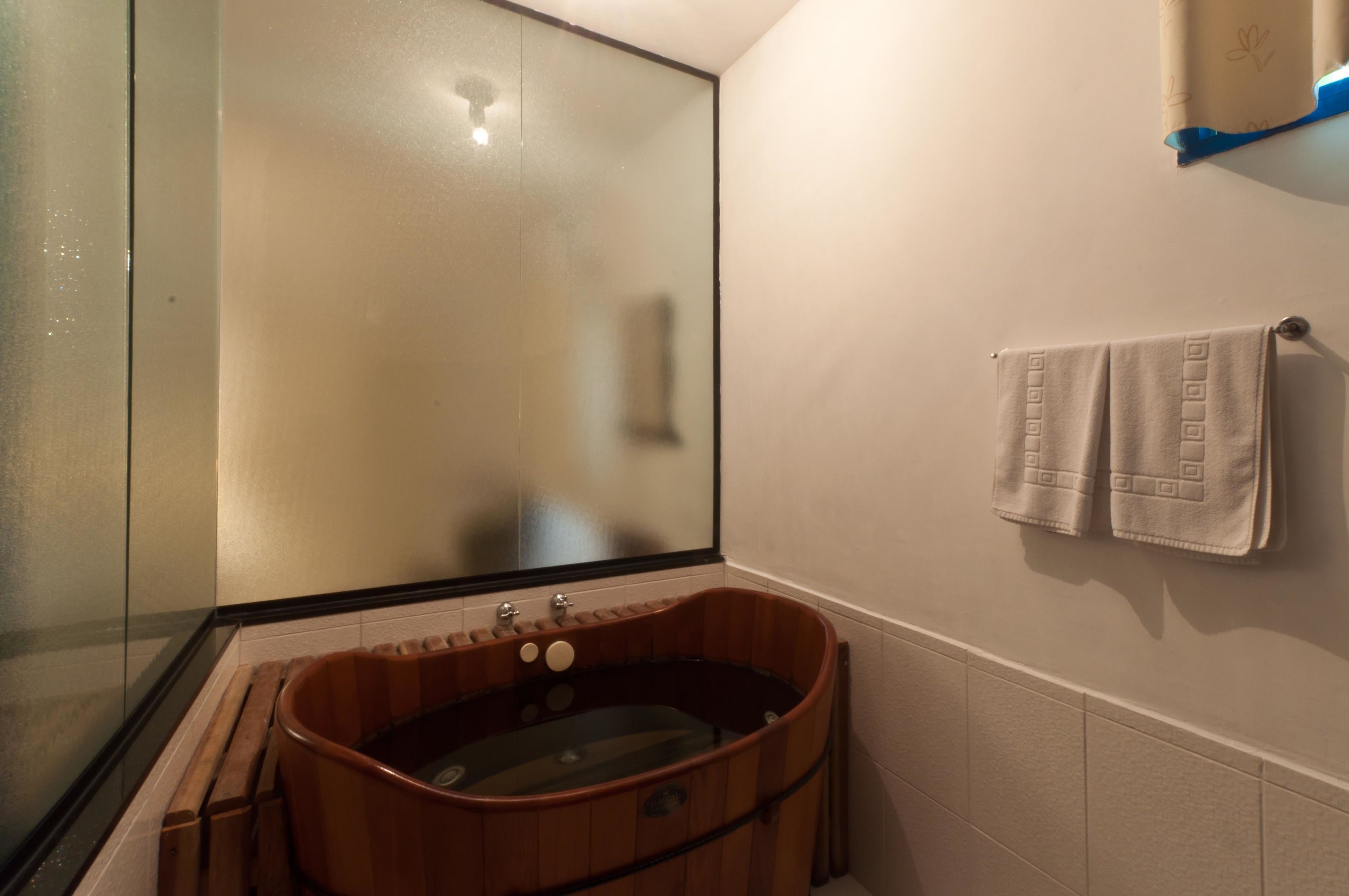Une salle de bain avec une baignoire en bois, une cabine de douche en verre et un porte-serviettes avec deux serviettes.
