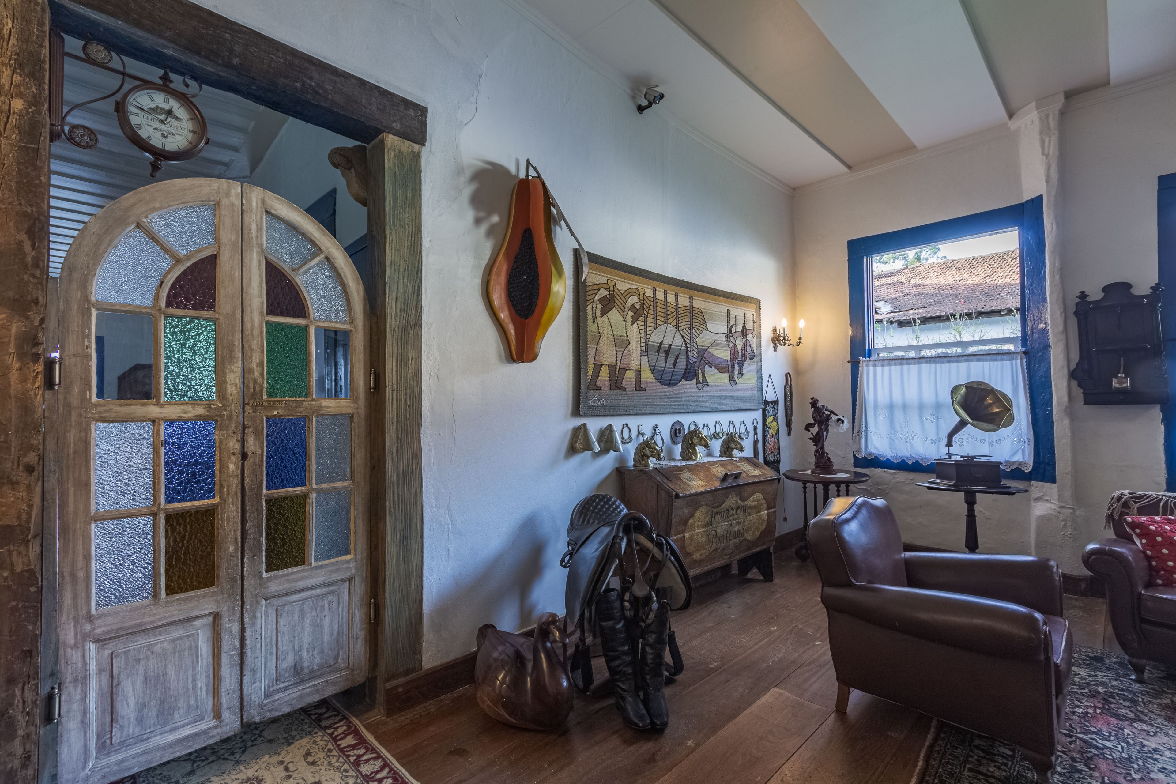 Une pièce avec une porte en bois ornée de panneaux de vitrail, une horloge, un objet décoratif fixé au mur, un gramophone ancien et un fauteuil en cuir.