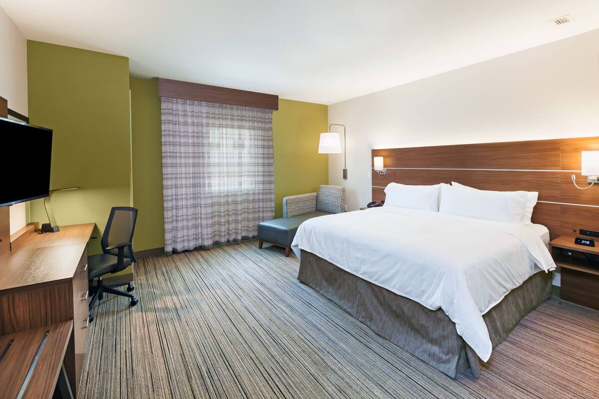 A hotel room with a bed, desk, chair, and a television.