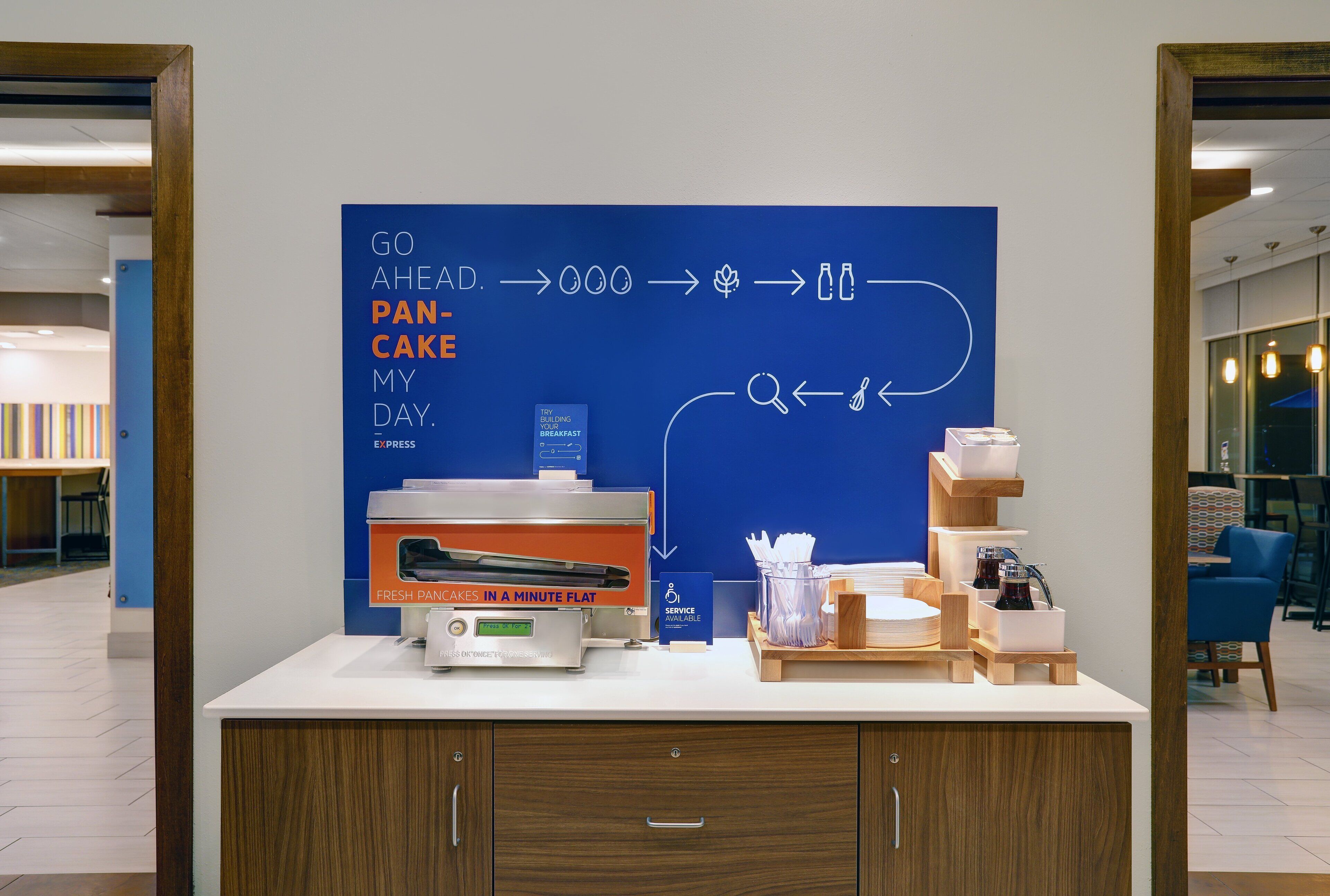 A breakfast station with a flat-screen TV displaying a breakfast menu, a coffee machine, and a sign indicating service availability.