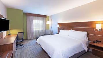 A hotel room with a bed, desk, chair, TV, and a nightstand with a lamp.