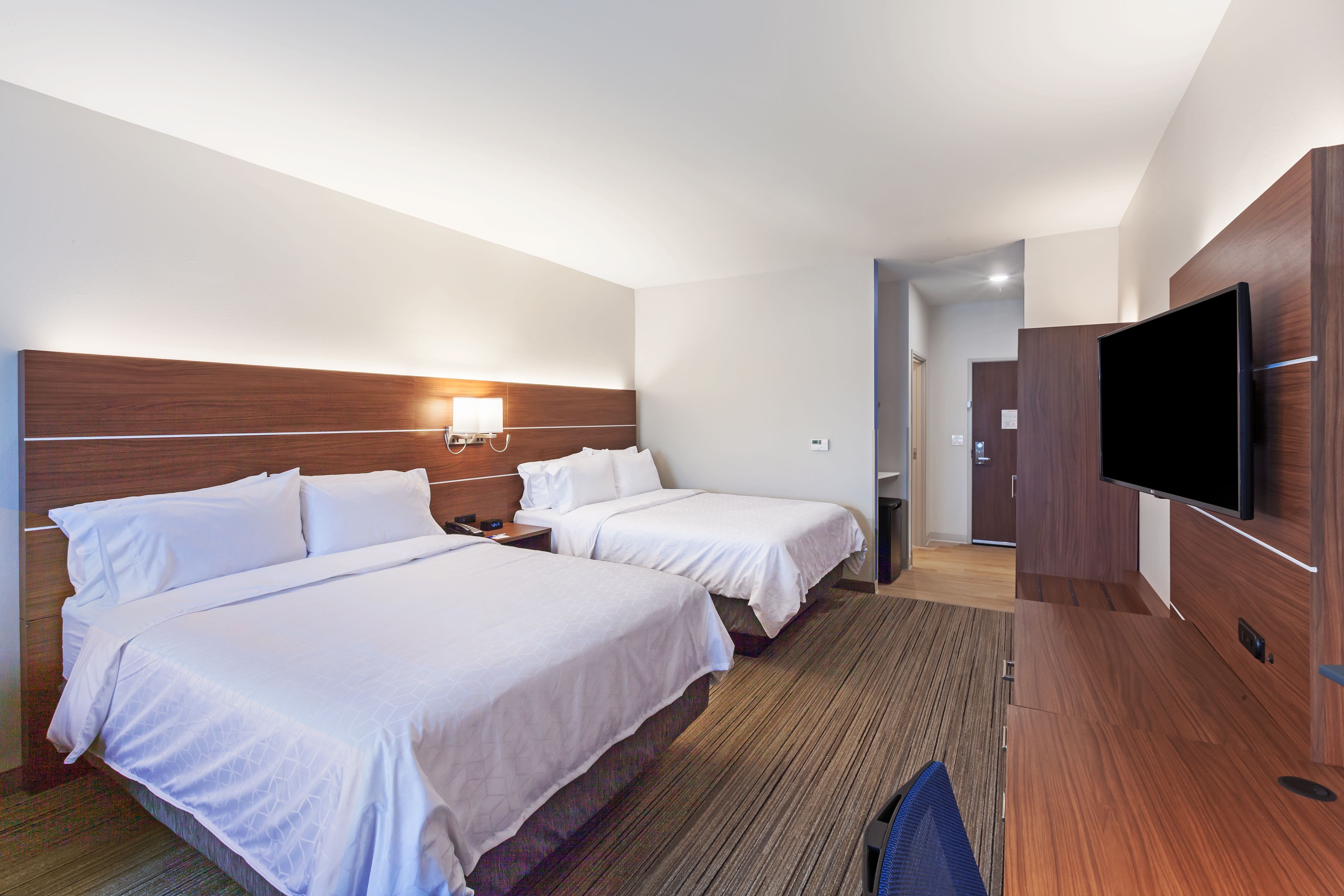 A hotel room with two beds, a flat-screen TV, a desk, and a walk-in closet.