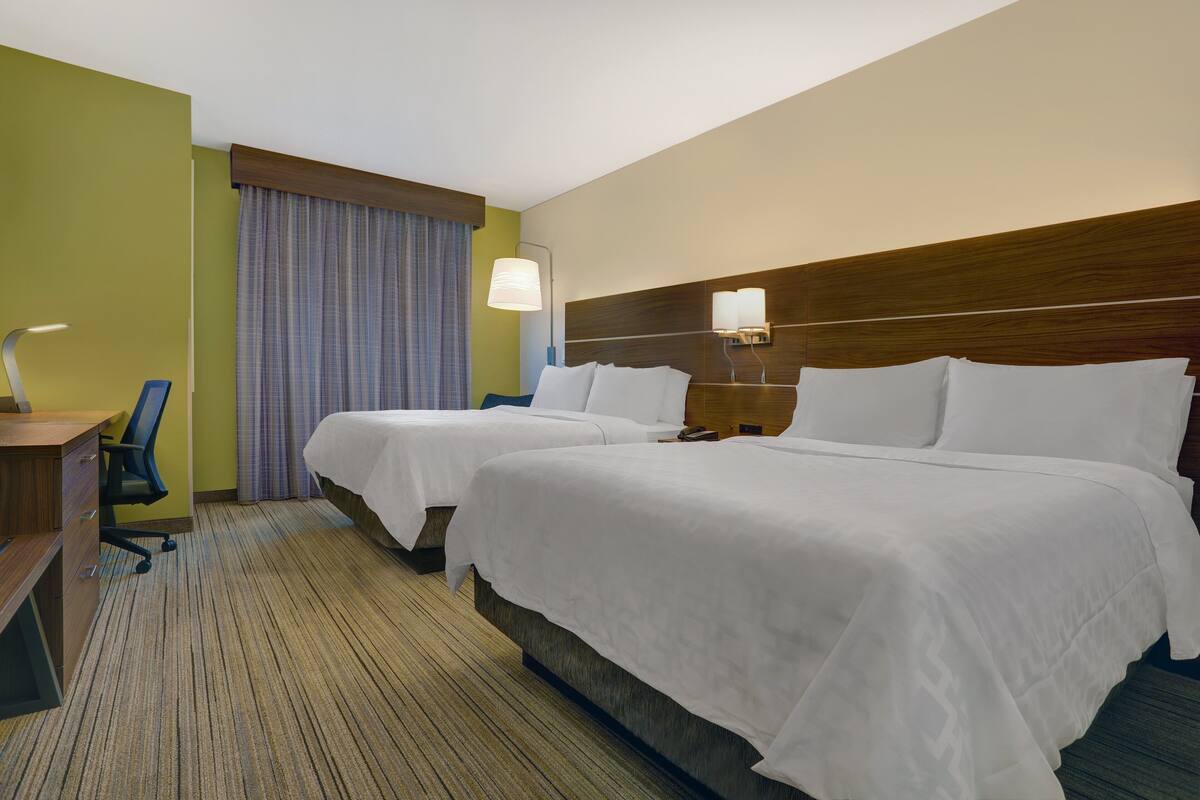 A hotel room with two beds, a desk, a chair, and a window with curtains.
