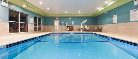 Una piscina interior con agua cristalina, una silla de salvavidas y un cartel con las normas de la piscina.