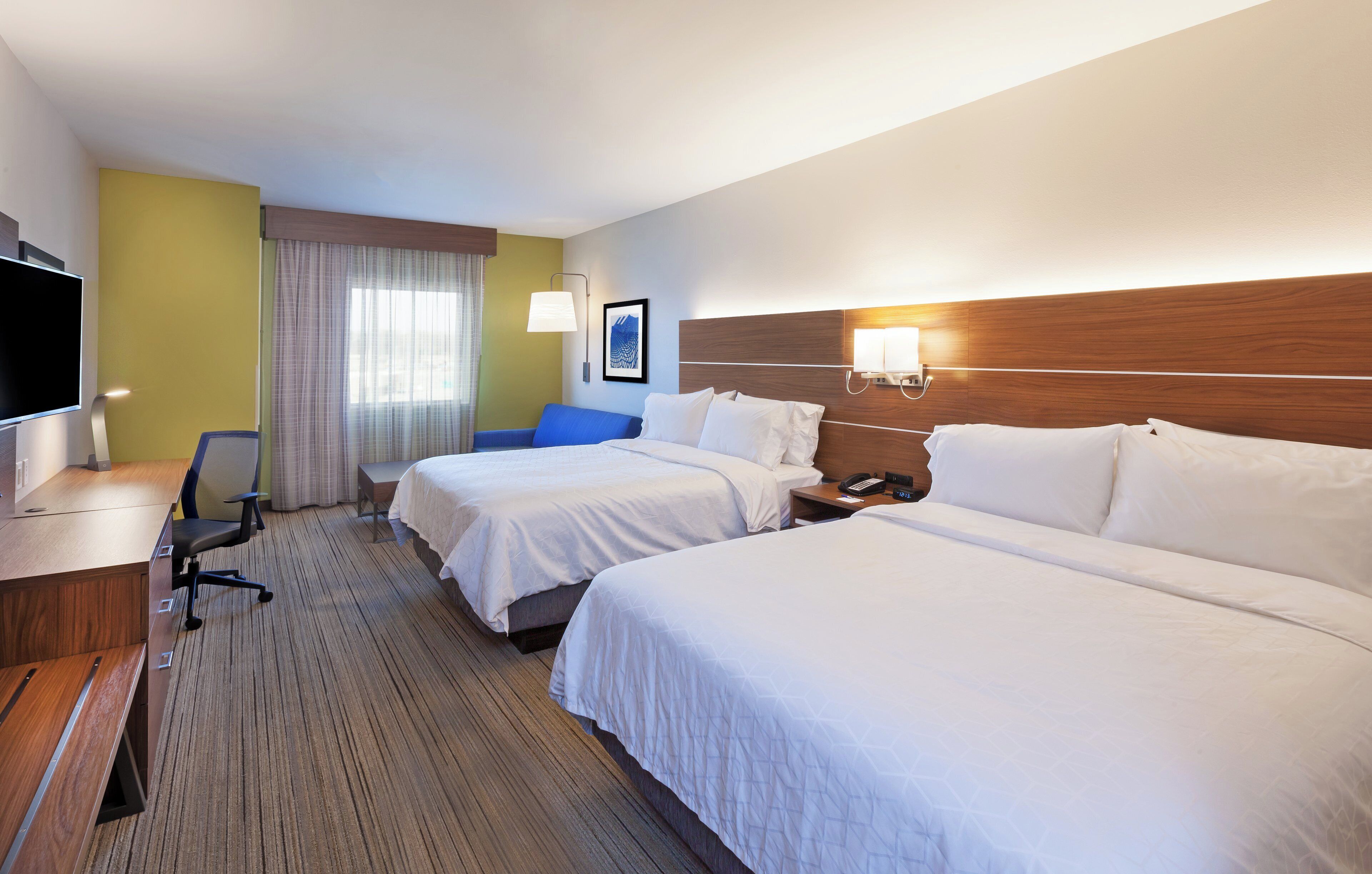 A hotel room with two beds, a desk, a chair, a TV, and a window with curtains.