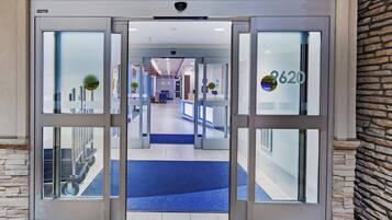 A hotel entrance with automatic doors, a reception desk, and a view into the lobby area.