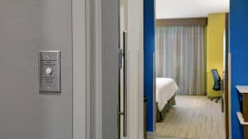 A hotel room with a bed, a desk, and a chair. There is a door with a sign indicating an audio-visual alert system for hearing-impaired guests.