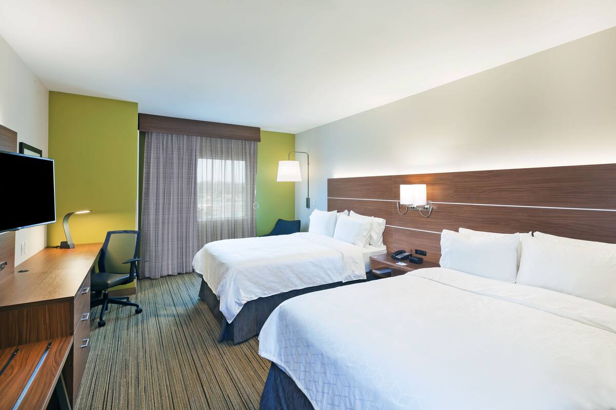 A hotel room with two beds, a desk, a chair, a TV, and a window with curtains.